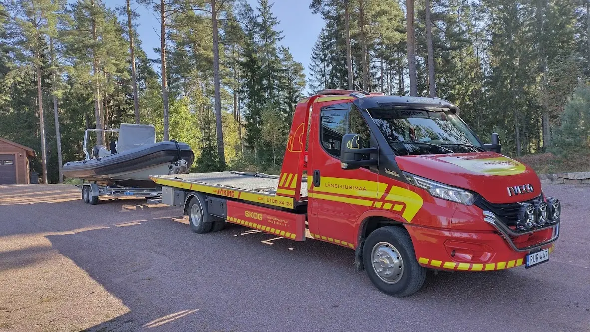 HinausPalvelu Skogin Iveco-merkkinen, Viking Hinauksen punakeltaisessa värityksessä oleva liukulavahinausauto vetää perässään venettä.